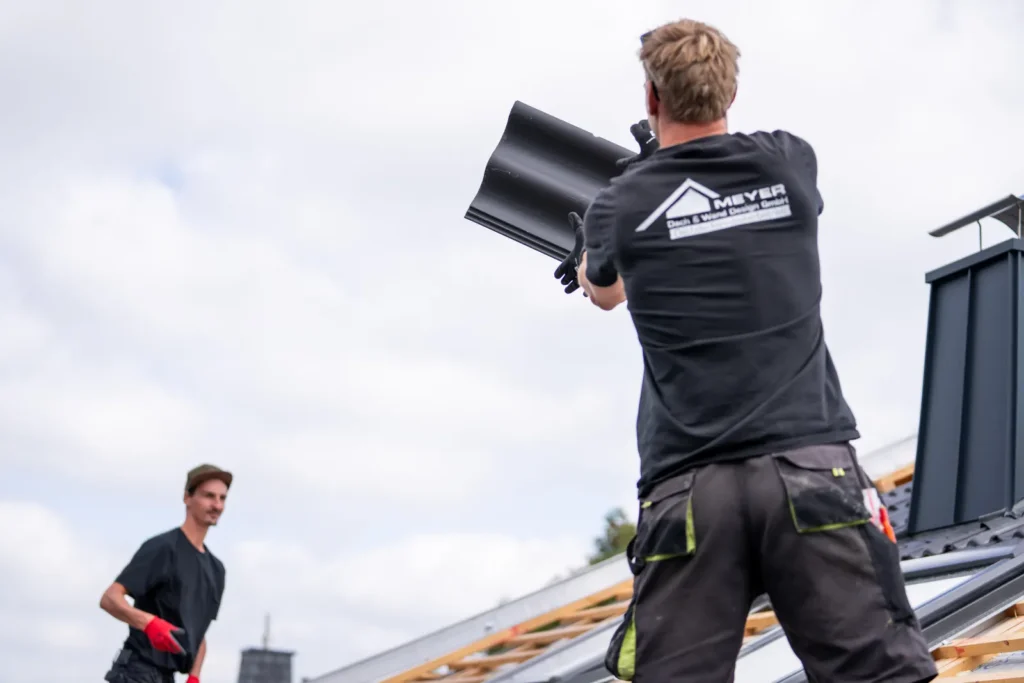 Dachdecker der Meyer Dach & Wand Design GmbH reicht einen anthrazitfarbenen Dachziegel an